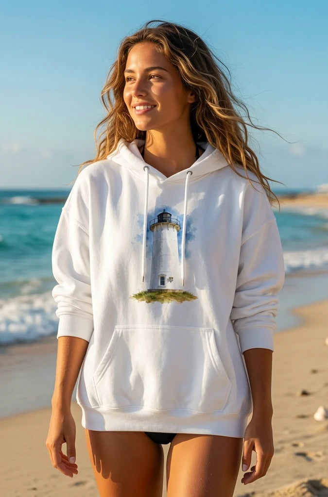 Woman wearing a white Cape Cod Lighthouses – Nobska Light Watercolor Coastal Hoodie with a lighthouse design on a beach