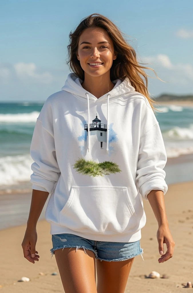 Woman wearing a white Cape Cod Lighthouses – Wood End Lighthouse Watercolor Coastal Hoodie with a lighthouse design on a beach